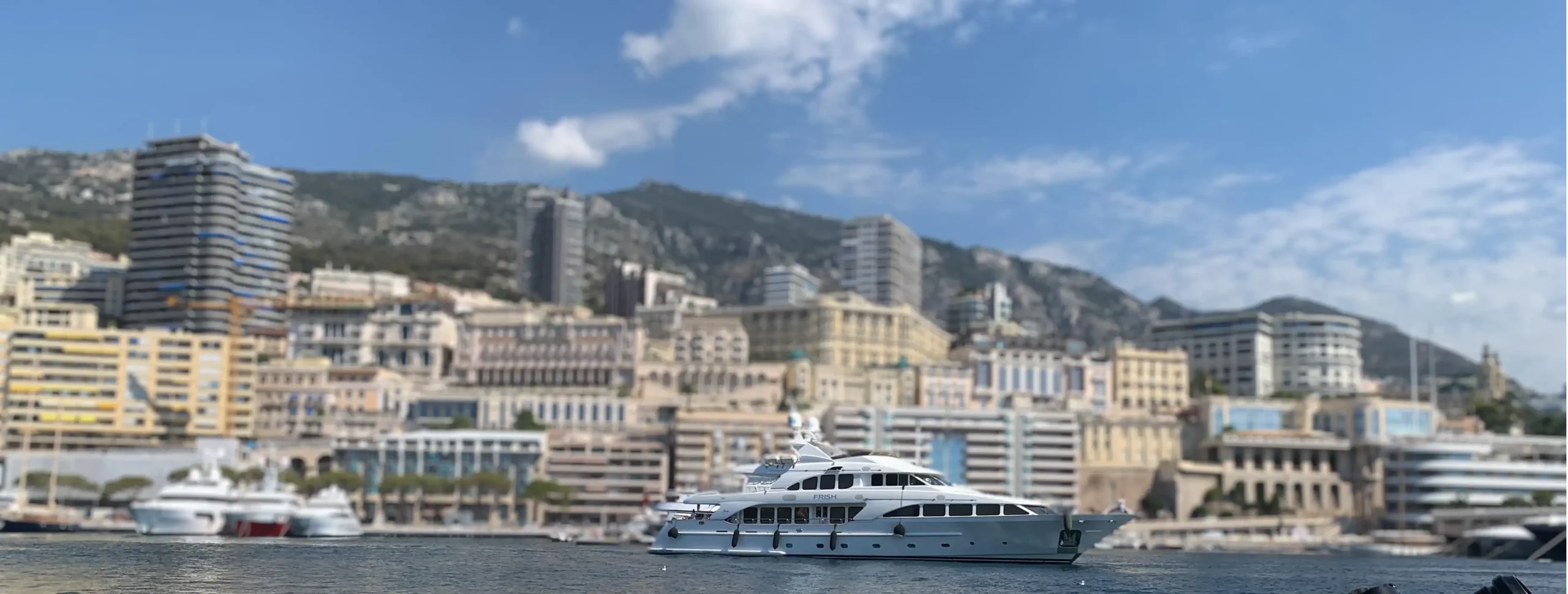 Bateau amarré dans le port de Monaco, avec des yachts de luxe et la vue sur les montagnes